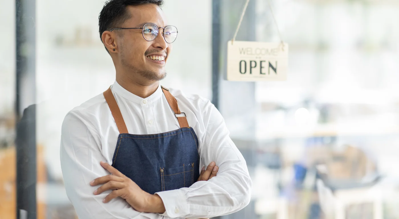 Smiling café owner in an apron standing by an open sign