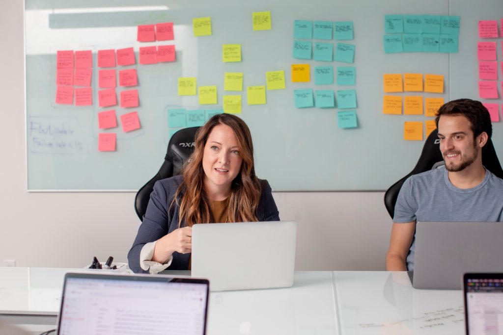 Employees sat at laptops in front of whiteboard and post it notes