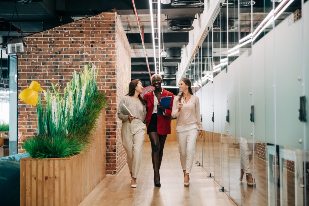 three women walk down modern office hallway