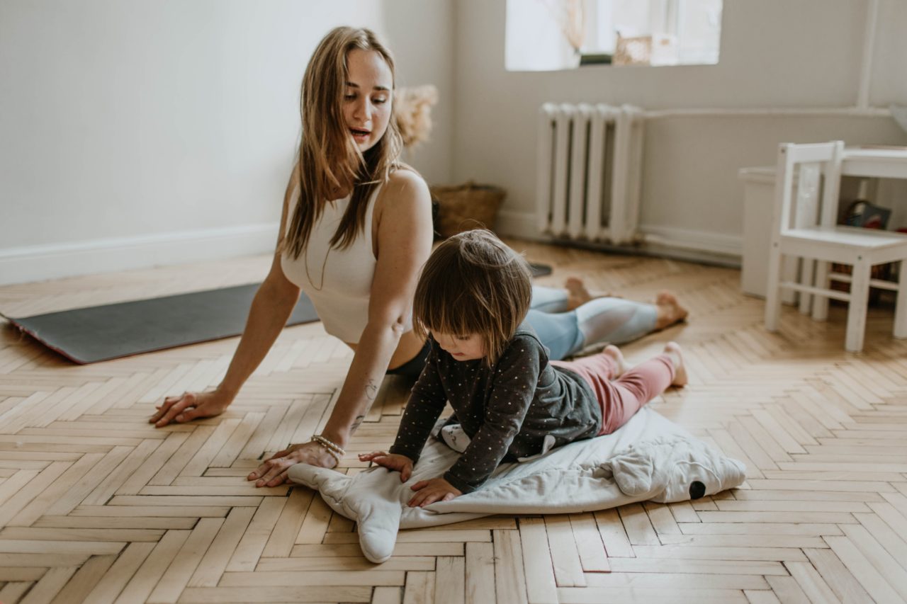 A woman does yoga at home with a toddler.