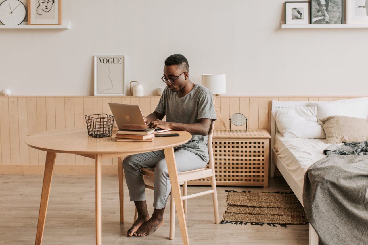 Man works on laptop at table close to his bed