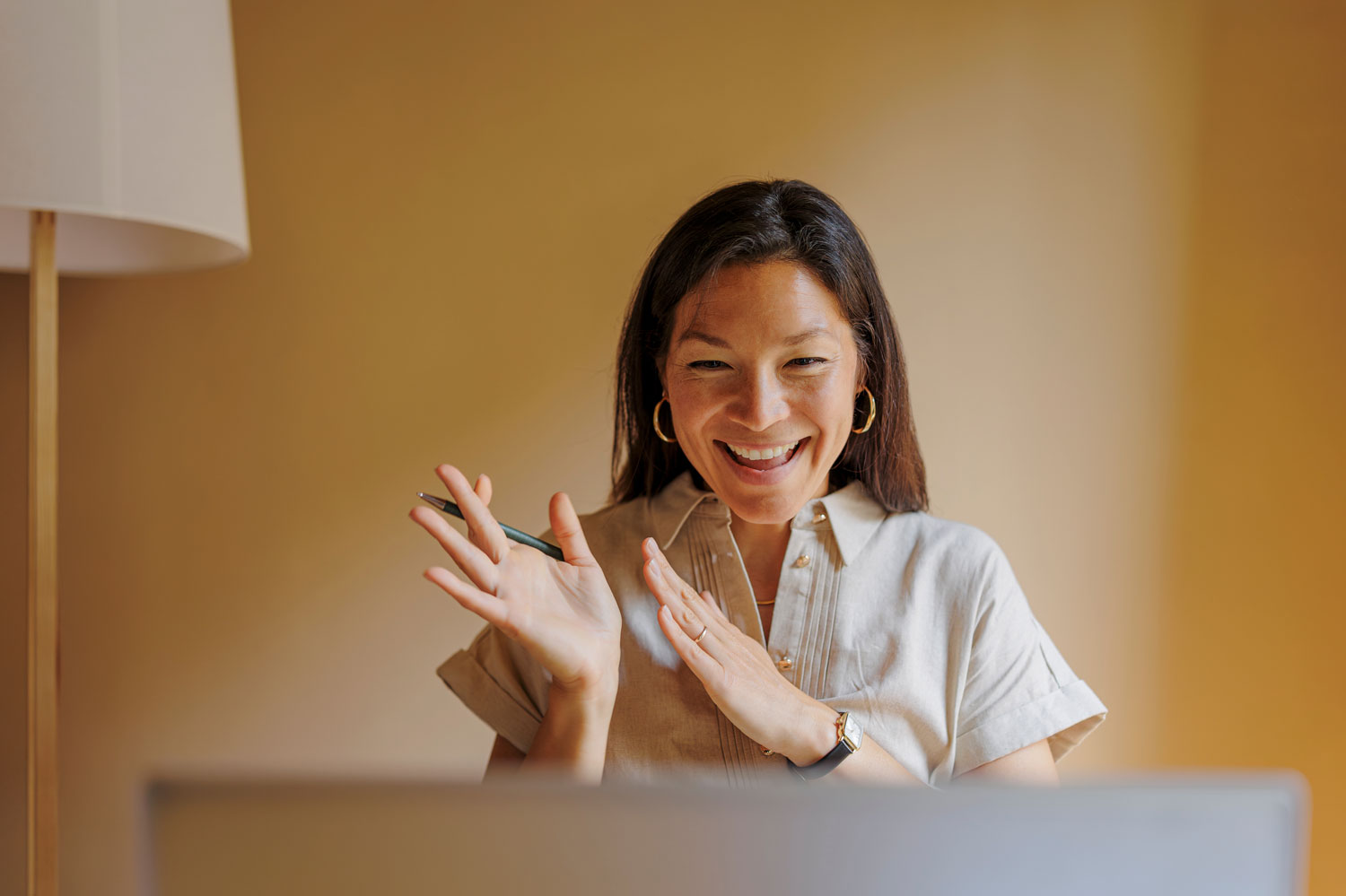 A smiling woman gesturing expressively during a video call at a warmly lit home desk, illustrating engaged remote employee communication.