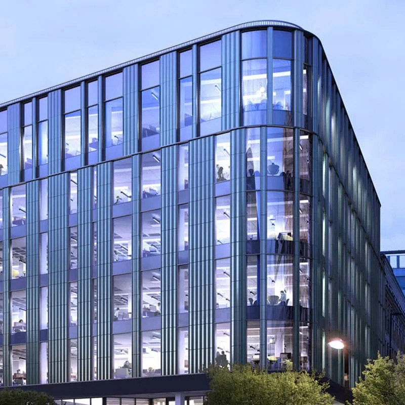 Close-up exterior rendering of Interact's Manchester HQ at dusk, a curved multi-story glass office building with illuminated workspaces visible across multiple floors.
