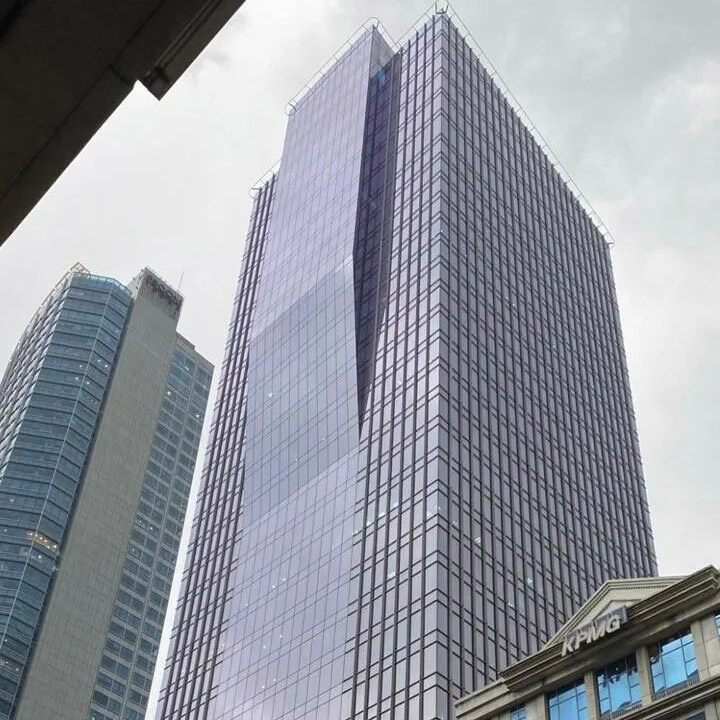 Upward view of a tall glass skyscraper in the Philippines with a KPMG office building visible at street level, set against an overcast sky.