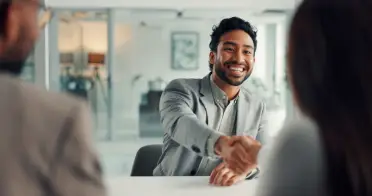 A smiling man in a gray suit shaking hands across a desk, representing a positive relationship.