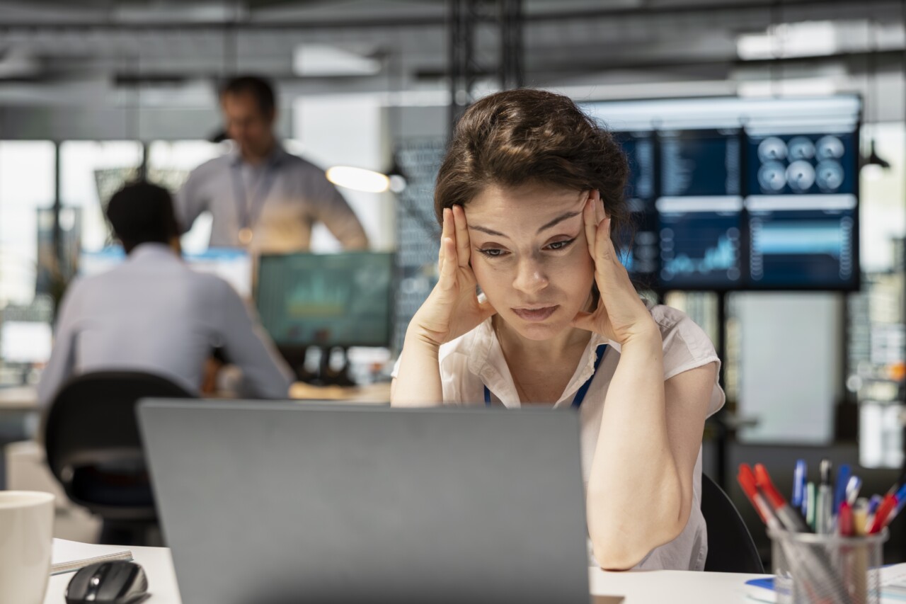 An employee holds her head in her hands as she sits at a laptop.