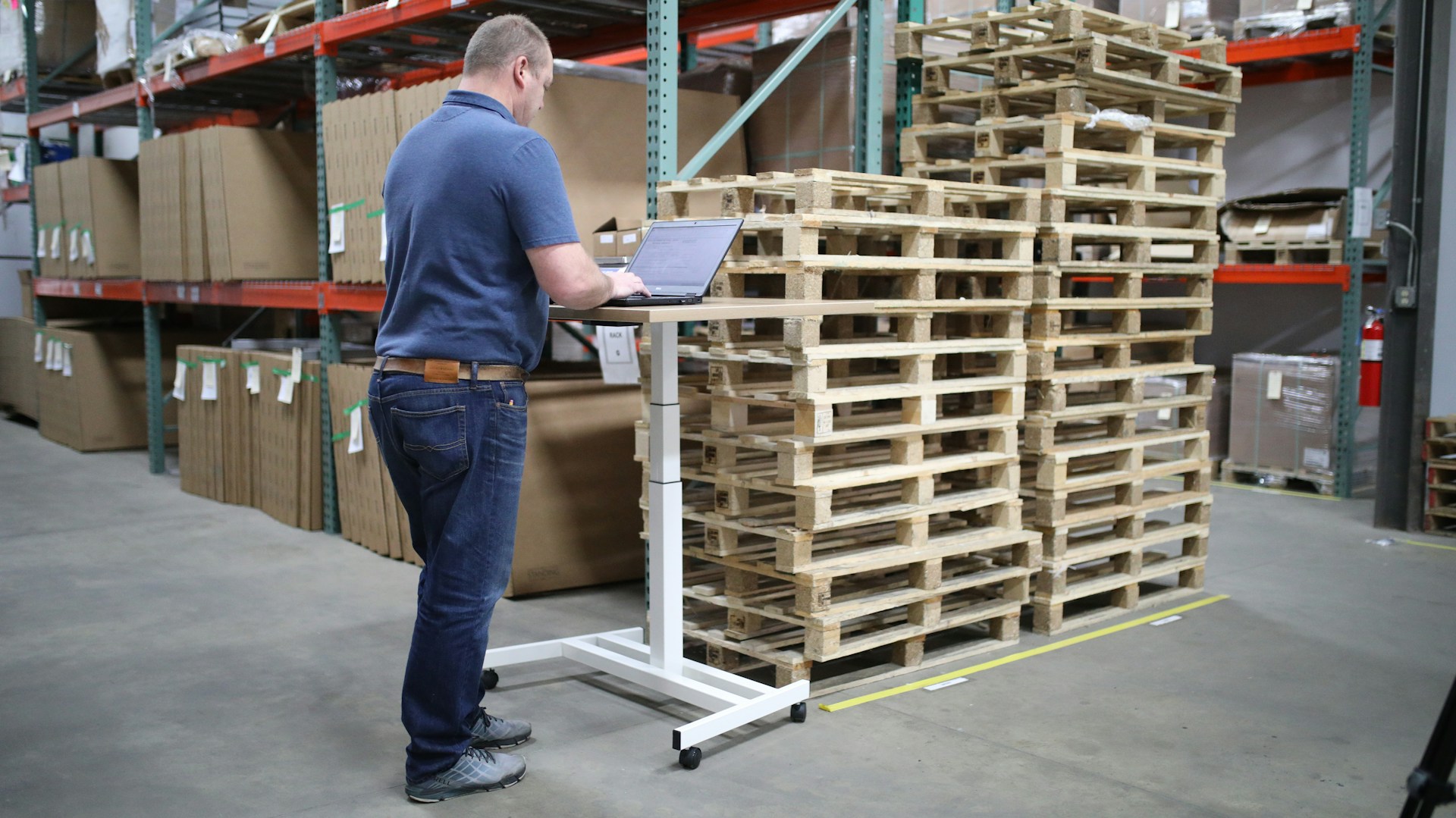 A warehouse worker uses the intranet from a standing desk next to a pile of pallets, showing why intranet AI capabilities must adapt to employee context.