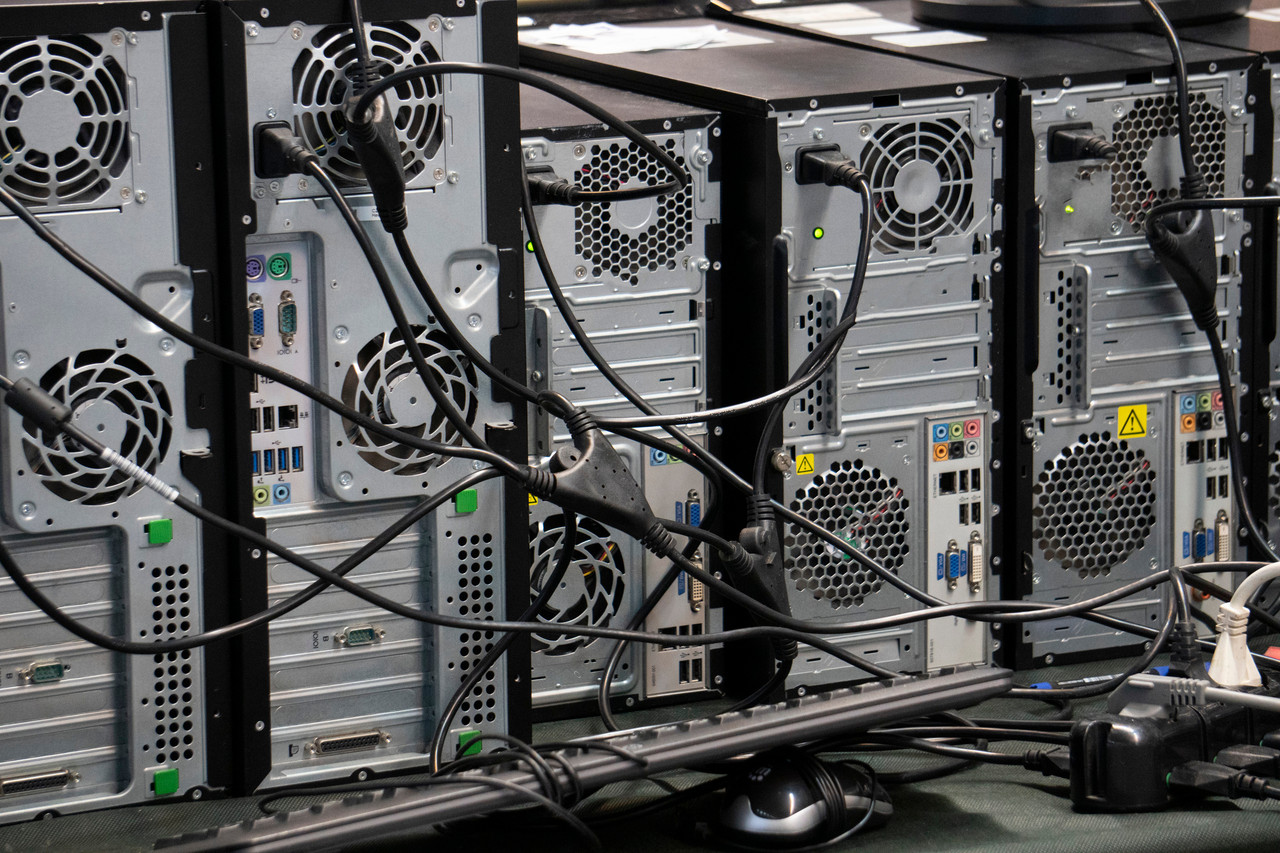 The rear side of multiple PC towers, with wires criss-crossed and tangled.